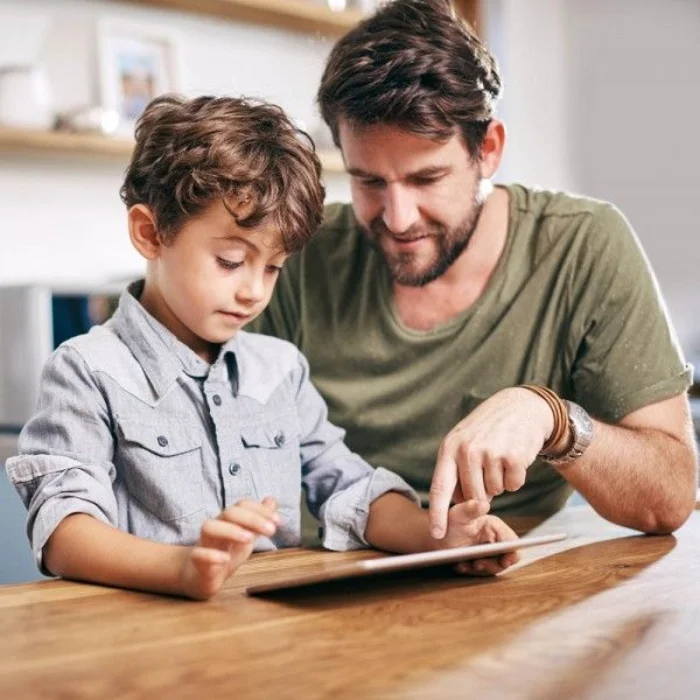 Padre acompañando a su hijo mientras usa la tablet